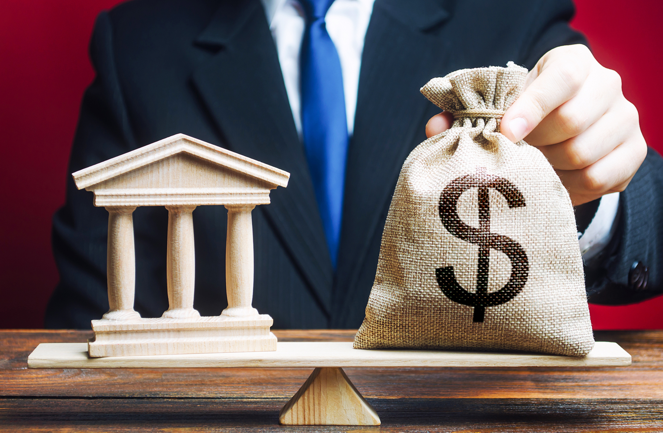 A man puts a money bag on scales opposite to building of government, bank, university. Budget and funding for normal functioning. Lobbying interests. Payment of taxes. Deposits and loans. Government and Money